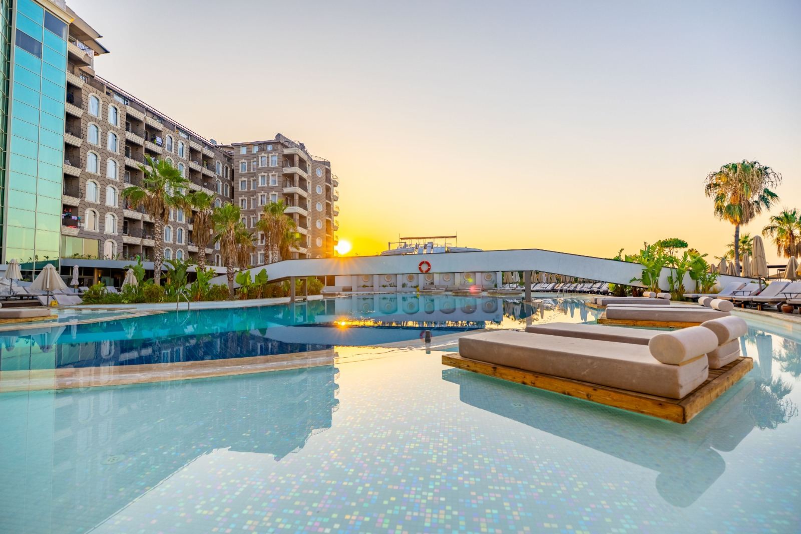 Resort swimming pool at sunset with palm trees and floating loungers
